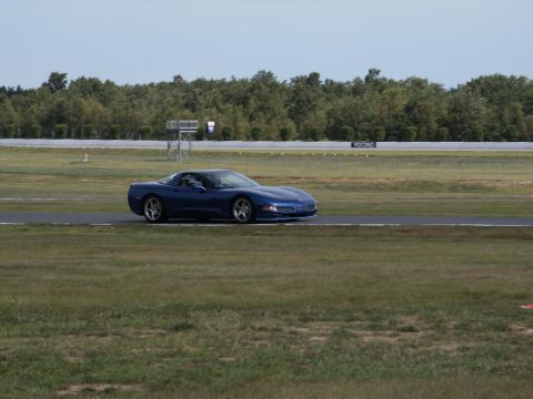 2001 Mercury Grand Marquis - Blue Chevrolet Corvette C5 coupe driving on a race track with trees in the background.