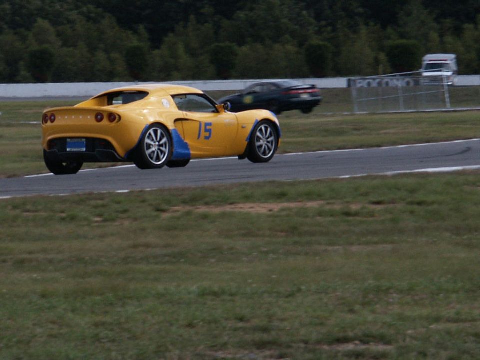 Yellow sports car with blue accents and number 15 on a race track, another dark car in the background