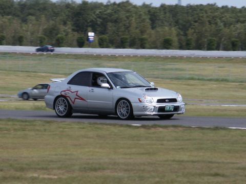2001 Mercury Grand Marquis - A silver Subaru Impreza WRX with a racing graphic drives on a track, with another car visible in the distance.