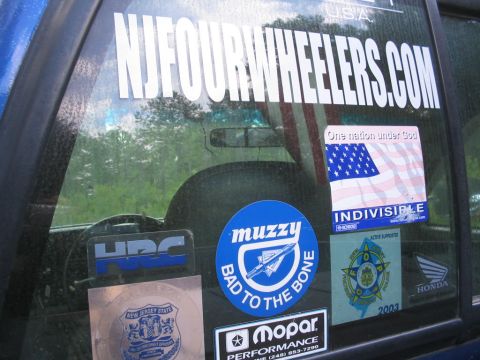 1990 Ford Bronco - A collection of stickers adorns the window of a blue vehicle, obscuring the interior and the view outside.