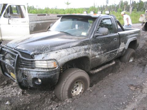 1990 Ford Bronco - This black pickup truck is deeply stuck in mud, with another vehicle visible in the background.