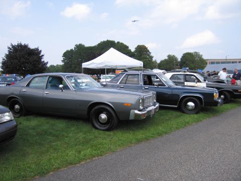 2001 Ford Crown Victoria - A lineup of vintage police cruisers, including a gray sedan and darker models, are displayed outdoors.