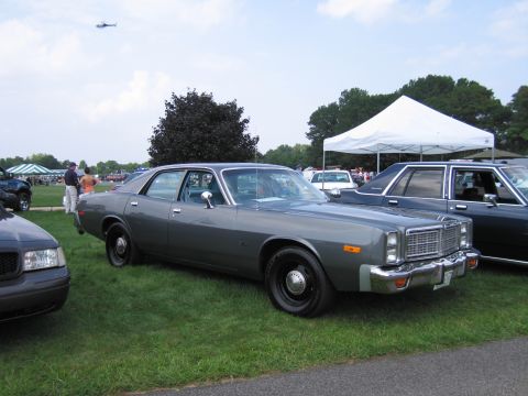 2001 Ford Crown Victoria - A vintage police sedan is parked on a grassy field next to other vehicles under a white tent.