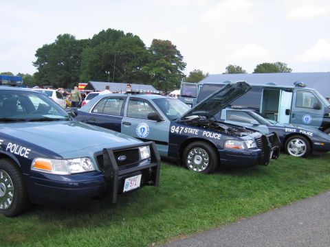 2001 Ford Crown Victoria - Several state police vehicles, including a Ford Crown Victoria with its hood open, are displayed on a grassy area.