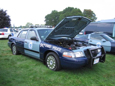 2001 Ford Crown Victoria - A police car with its hood open, displaying the engine, sits on a grassy field next to another police vehicle.