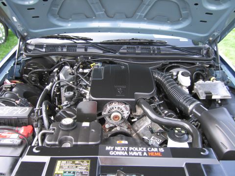 2001 Ford Crown Victoria - The engine compartment of a vehicle is shown, a prominent sticker with a humorous message about future police cars.