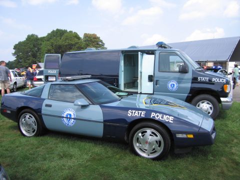 2001 Ford Crown Victoria - Massachusetts State Police Corvette and van displayed outdoors on a grassy field under a partly cloudy sky.