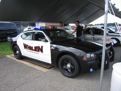 2001 Ford Crown Victoria - Police car with Whelen branding and emergency lights is displayed under a tent at an event.