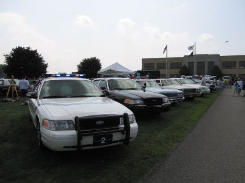 2001 Ford Crown Victoria - Several police cars are lined up on a grassy area in front of a building.