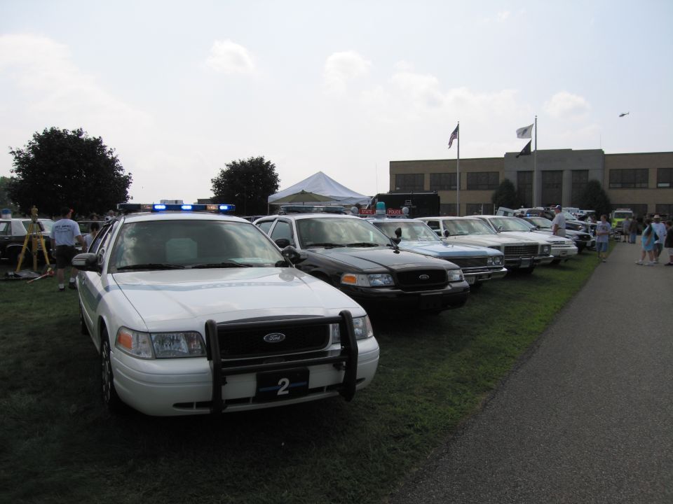 White 2001 Ford Crown Victoria police car with light bar and push bumper, parked on grass