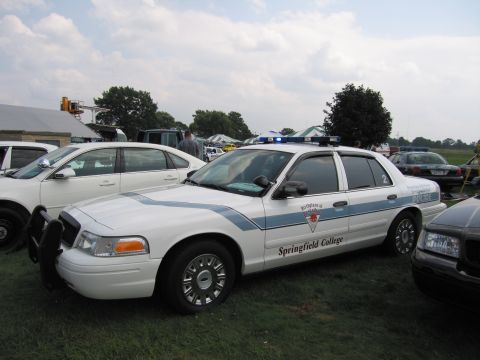 2001 Ford Crown Victoria - A 2001 Ford Crown Victoria police car, marked for Springfield College, is parked on grass with blue lights illuminated.