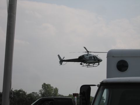 2001 Ford Crown Victoria - A helicopter is seen in the sky, partially obscured by a large white structure and the top of a truck.