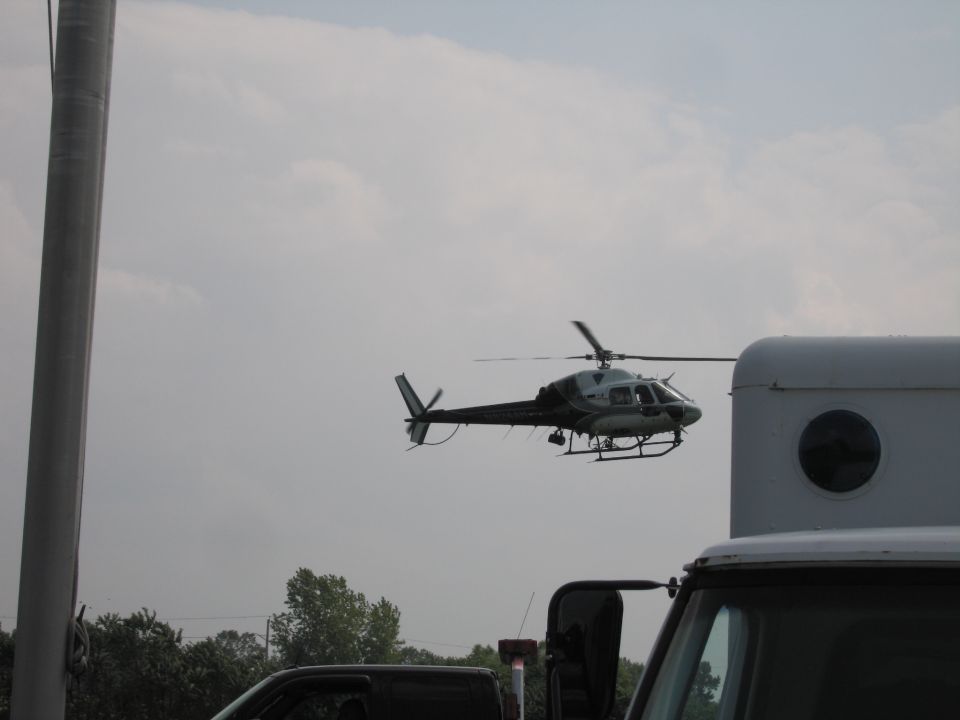 Helicopter flying near a large white structure and the top of a truck
