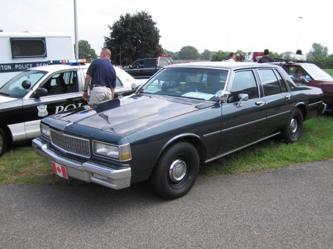 2001 Ford Crown Victoria - A dark green sedan, likely from the 1980s, is parked next to a police vehicle.