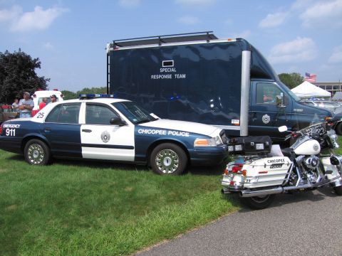 2001 Ford Crown Victoria - A police car, a special response truck, and a police motorcycle are parked together on a grassy area.