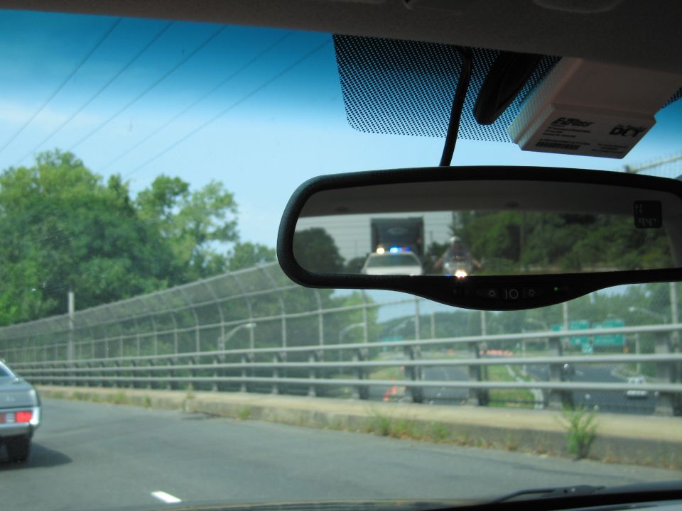 Police car with flashing blue lights reflected in a rearview mirror, seen from inside another vehicle