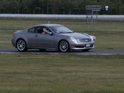 2001 Mercury Grand Marquis - A silver coupe with a driver wearing a racing helmet drives on a race track, with another vehicle in the background.