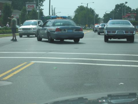 2001 Ford Crown Victoria - Police car with lights active, seen from behind on a multi-lane road with other traffic.