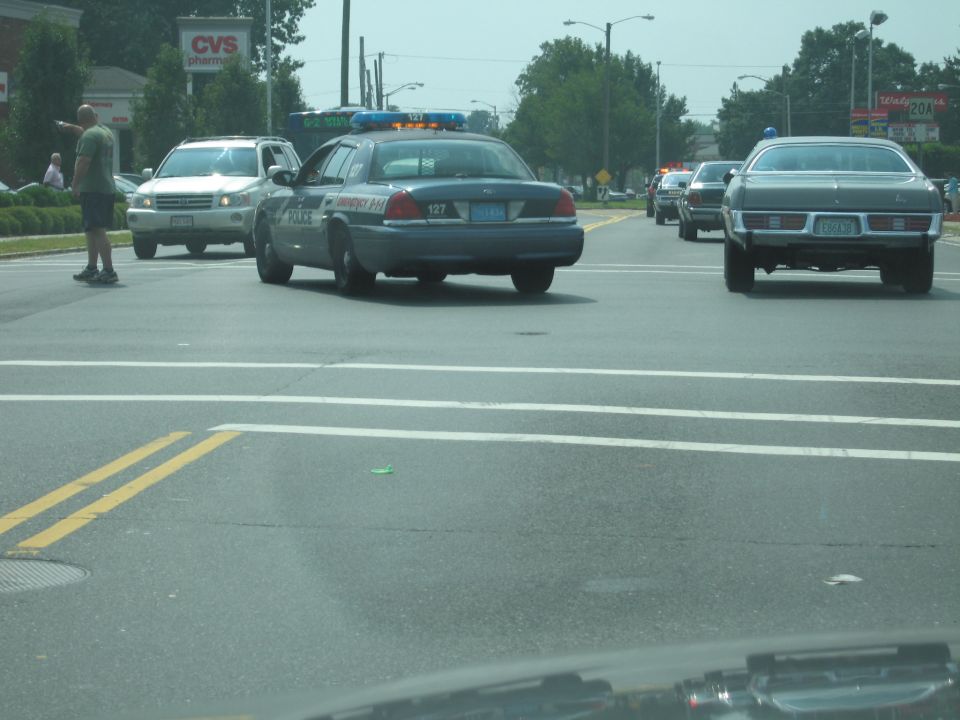 2001 Ford Crown Victoria police car with lights on, driving on a street with other cars