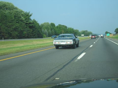 2001 Ford Crown Victoria - A vintage sedan drives down the highway on a clear day, with other vehicles visible in the distance.
