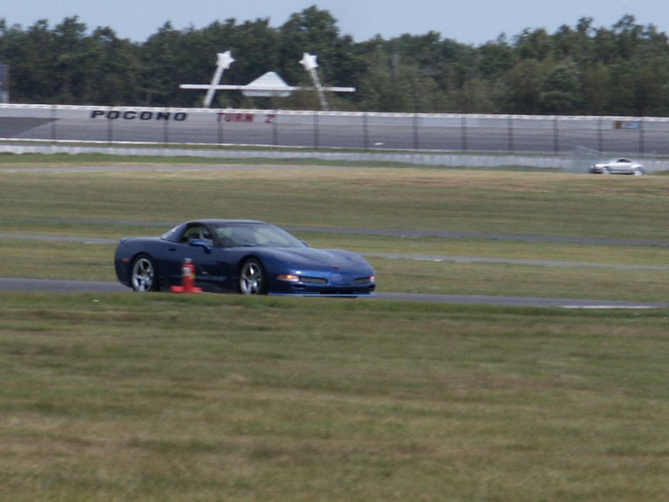Blue Chevrolet Corvette C5 on a race track with a white car in the distance