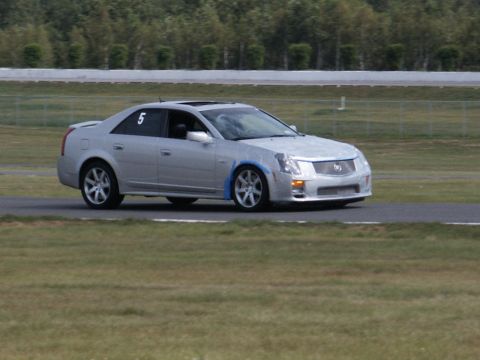 2001 Mercury Grand Marquis - A silver Cadillac CTS with racing number 5 is on the track, with trees and a fence in the background.