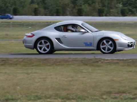 2001 Mercury Grand Marquis - A silver Porsche Cayman with the number 762 on its side drives on a race track, with another blue car in the background.
