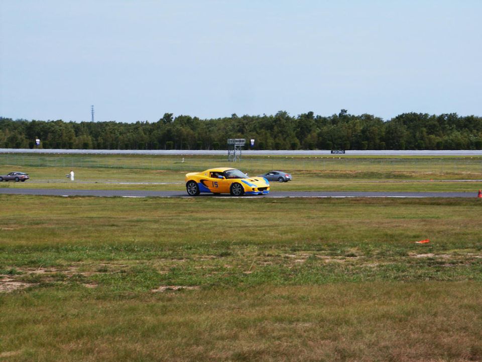Yellow sports car with blue accents and number 15 on a race track, another car in the background