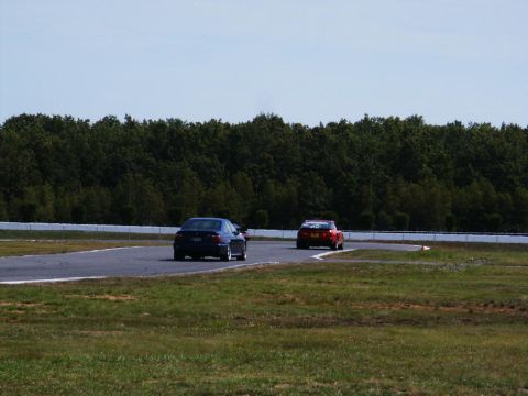 2001 Mercury Grand Marquis - Two cars race on a track with a wooded background and a bright blue sky.