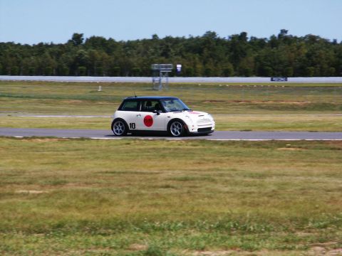 2001 Mercury Grand Marquis - A white Mini Cooper with racing decals is seen on a race track under a clear sky.