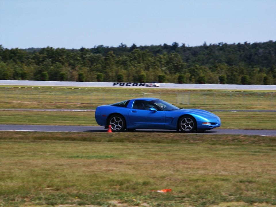 Blue Corvette C5 on a racetrack. The word 'Pocono' is visible on a sign in the background