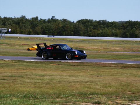 2001 Mercury Grand Marquis - A black Porsche 911 with a prominent rear spoiler and red interior is seen on a race track, with another yellow car in the background.