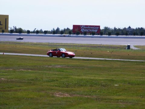 2001 Mercury Grand Marquis - A red convertible speeds around a race track, with another car in the distance and a large Budweiser Racing sign overhead.
