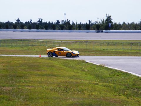 2001 Mercury Grand Marquis - A yellow sports car navigates a turn on a paved race track with grassy verges.