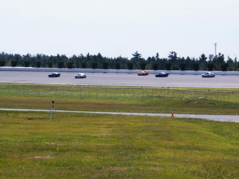 2001 Mercury Grand Marquis - Cars are seen on a race track with a grassy foreground and a line of trees in the distance.