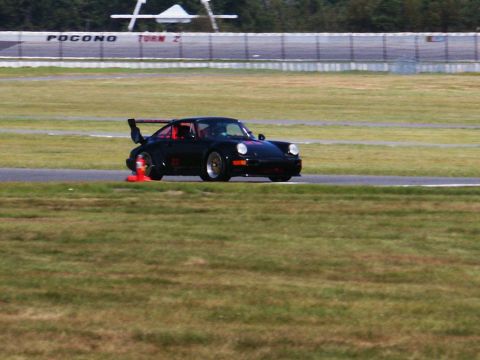 2001 Mercury Grand Marquis - A black Porsche 911 with a prominent rear spoiler navigates a turn on a race track, with 'Pocono Turn 2' visible in the background.