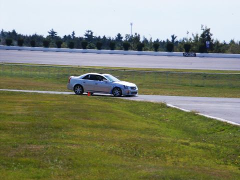 2001 Mercury Grand Marquis - A silver Cadillac CTS-V is seen on a race track with a white wall and trees in the background.