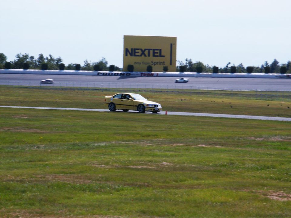 Yellow BMW E36 sedan on race track, Nextel billboard in background