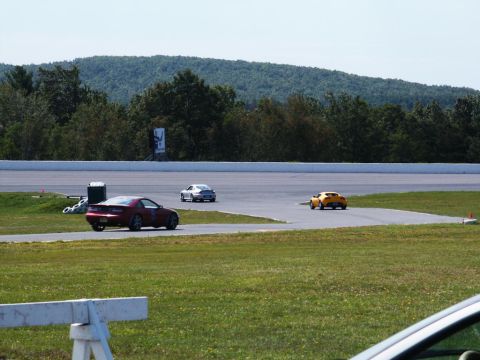 2001 Mercury Grand Marquis - Three cars are on a race track during a sunny day, with trees and hills in the background.