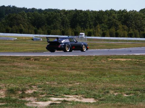 2001 Mercury Grand Marquis - A black racing car with a prominent rear spoiler and gold wheels navigates a turn on a sunny day at a racetrack.