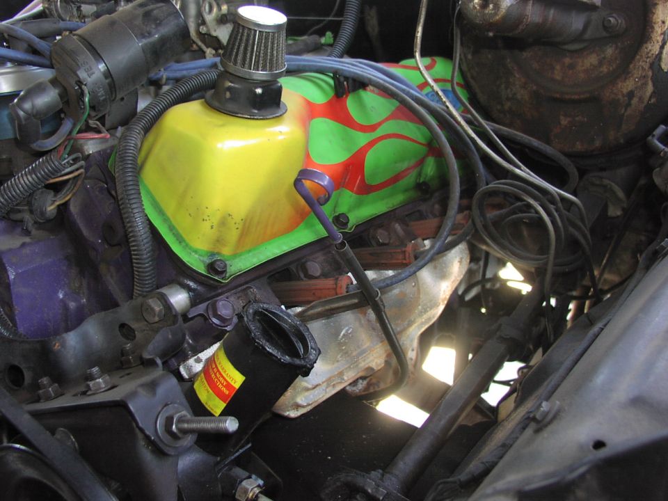 Engine bay with a yellow valve cover painted with green and red flames. A small air filter is on top