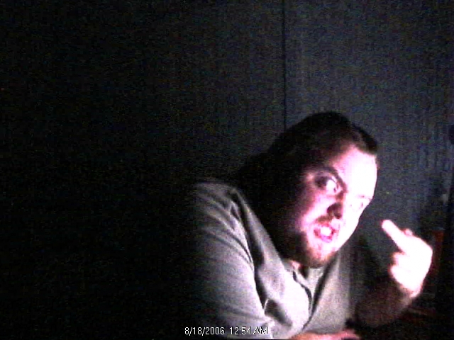 Man with beard and angry expression, giving the middle finger, with a timestamp and website overlay