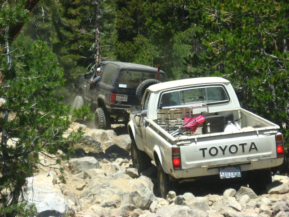 White Toyota pickup truck and black SUV on a rocky trail, both with off-road tires