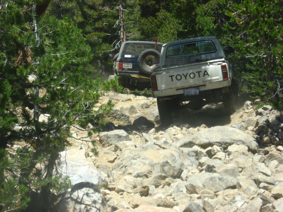 White Toyota pickup truck and dark SUV on a rocky mountain trail