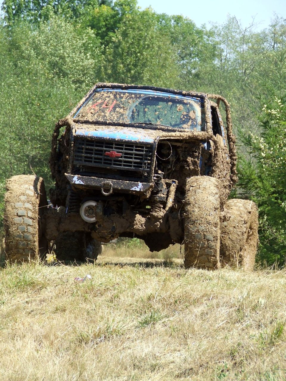 Mud-covered off-road vehicle with a black grille and red emblem, front view