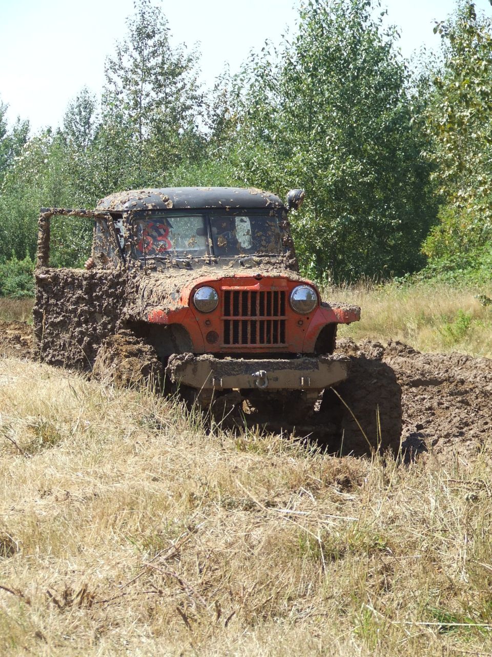 Mud-caked orange vintage 4x4 with vertical-slat grille and number 63 in a mud pit