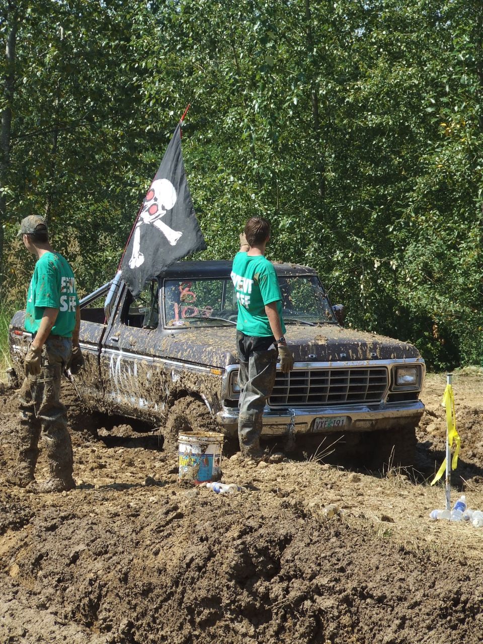Mud-covered Ford pickup stuck in mud with pirate flag and event staff nearby