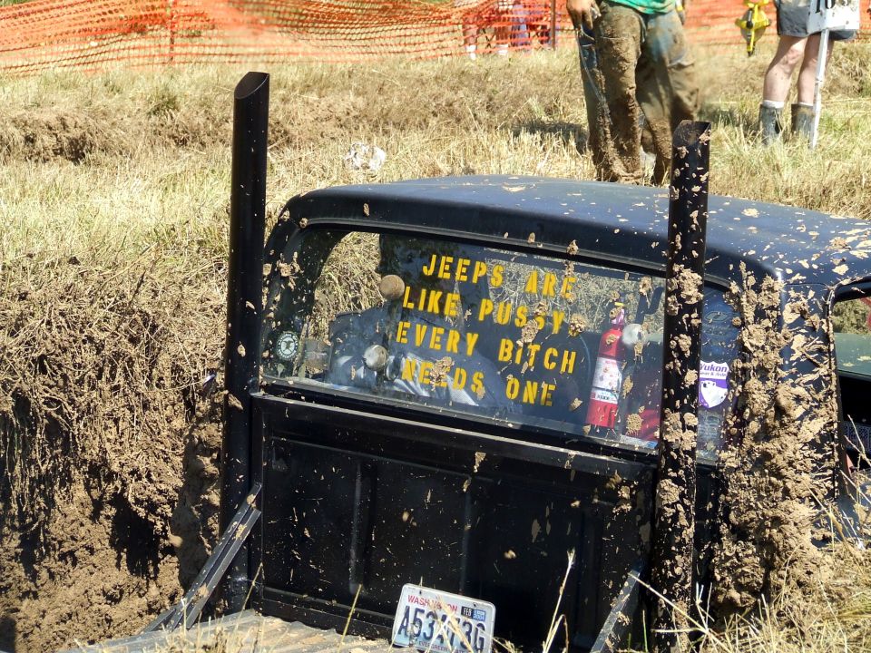 Muddy black pickup stuck in a mud pit, rear window decal, Washington plate.