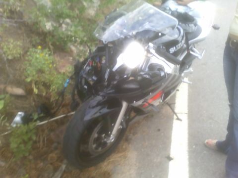 1996 Ford Probe - A damaged black Suzuki sportbike is partially off the road, with its front fairing and lights in disarray.