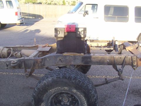 1978 Ford Bronco - Focus on the chassis and suspension components of a vehicle, with a van in the background.